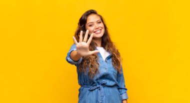 Kız gülümsüyor ve arkadaş canlısı görünüyor, 5 ya da 5 numarayı gösteriyor, elleri önde, geriye doğru sayıyor.