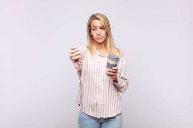 Kahve içen genç bir kadın kızgın, sinirli, hayal kırıklığına uğramış ya da hoşnutsuz, ciddi bir bakışla başparmağını kaldırıyor.