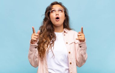 Kız şaşırmış, şaşırmış ve ağzı açık, iki eliyle boşluğu kopyalamak için yukarı bakıyor.
