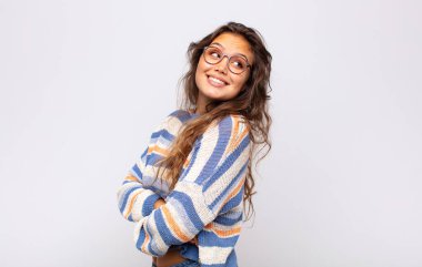 Kız neşeyle gülümsüyor, mutlu, tatmin olmuş ve rahatlamış hissediyor, kollarını kavuşturup yan tarafa bakıyor.