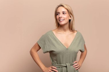 Mutlu, neşeli ve kendinden emin görünen, gururla gülümseyen ve iki elini de kalçasında taşıyan bir kadın.