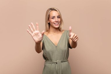 Gülümseyen ve arkadaş canlısı görünen bir kadın, 6 ya da 6 numarayı gösteriyor, elleri önde, geri sayıyor.