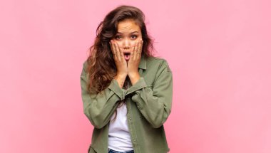 Kız şok olmuş ve korkmuş hissediyor, ağzı açık ve elleri yanaklarında korkmuş görünüyor.