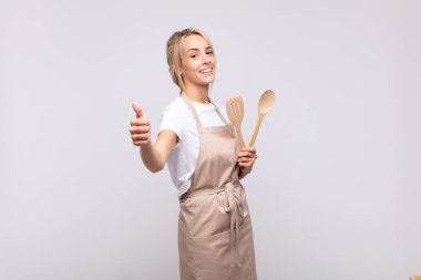 Genç kadın şef gururlu, tasasız, kendinden emin ve mutlu, başparmağıyla olumlu gülümsüyor.
