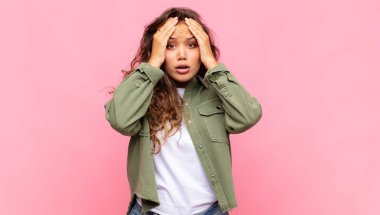 Kadın mutsuz, korkmuş ya da endişeli görünüyor, ağzı sonuna kadar açık ve iki kulağını da elleriyle kapatıyor.