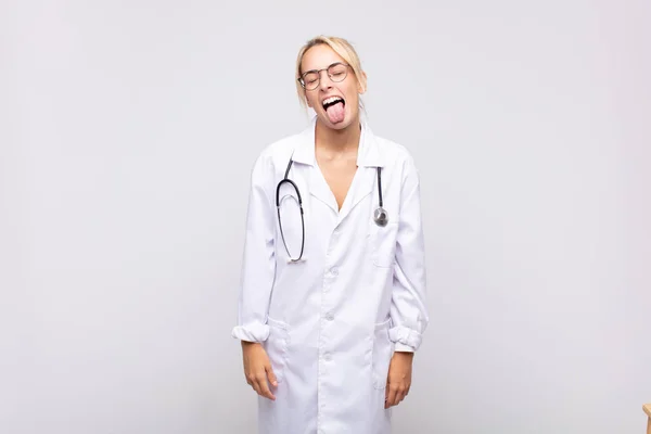 陽気で屈託のない反抗的な態度冗談を言いながら舌を出す若い女性医師は — ストック写真