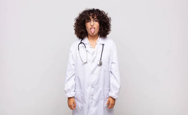 若い女性の医者はうんざりしていらいらして舌を出し嫌なことや幸運なことを嫌い — ストック写真