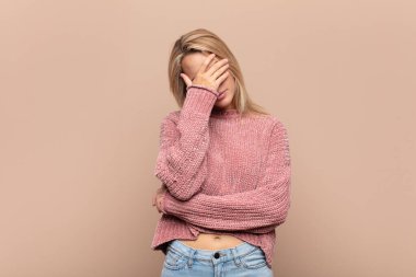 Stresli, utanmış ya da üzgün görünen bir kadın. Baş ağrısı var, yüzünü elleriyle kapatıyor.