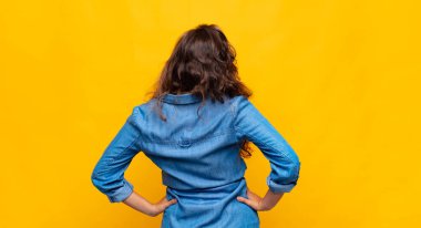 Kadın kafası karışık ya da dolu ya da şüphe ve soru dolu, merak ediyor, elleri kalçasında, dikiz aynasından