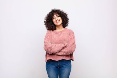 Mutlu, gururlu ve tatmin olmuş bir kadın gibi görünüyor. Kollarını kavuşturup gülümsüyor.