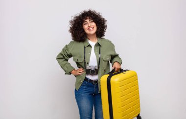 Genç Arap kadın mutlu bir şekilde gülümsüyor, eli kalçasında ve kendine güvenen, pozitif, gururlu ve arkadaş canlısı seyahat konseptiyle.