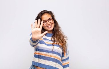 Gülümseyen ve arkadaş canlısı görünen bir kadın, 5 ya da 5 numarayı gösteriyor, eli önde, geri sayıyor.