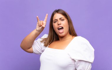 Genç sarışın kadın kendini mutlu, eğlenceli, kendinden emin, pozitif ve asi hissediyor, elle rock veya heavy metal işareti yapıyor.