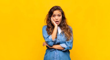 Şok ve inançsızlık içinde ağzı açık, elleri yanağı ve kolu çaprazlanmış, sersemlemiş ve şaşkın bir kadın.