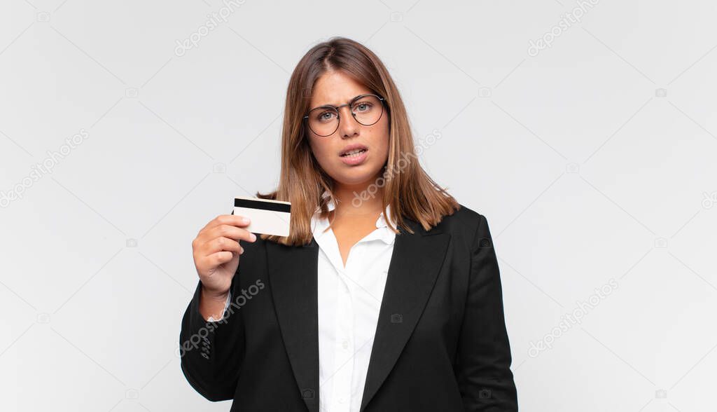 young woman with a credit card feeling puzzled and confused, with a dumb, stunned expression looking at something unexpected