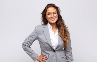 Kadın mutlu bir şekilde gülümsüyor, eli kalçasında ve kendinden emin, olumlu, gururlu ve arkadaş canlısı.