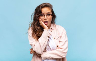 Şok ve inançsızlık içinde ağzı açık, elleri yanağı ve kolu çaprazlanmış, sersemlemiş ve şaşkın bir kadın.