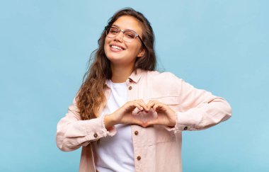 Gülümseyen ve mutlu hisseden bir kadın. Sevimli, romantik ve aşık. İki eliyle kalbi şekillendiriyor.