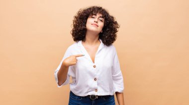 Gururlu, kendinden emin ve mutlu görünen, gülümseyen ve kendini gösteren ya da bir numaralı işareti yapan bir kadın.