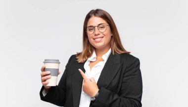 Kahveli genç iş kadını, neşeli bir şekilde gülümsüyor, mutlu hissediyor ve yan ve yukarı doğru işaret ediyor, fotokopi uzayında nesneler gösteriyor.