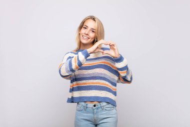 Gülümseyen ve mutlu hisseden bir kadın. Sevimli, romantik ve aşık. İki eliyle kalbi şekillendiriyor.