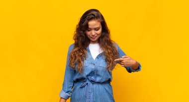 Neşeli bir şekilde gülümseyen, aşağıya bakan ve göğsünü gösteren bir kadın.