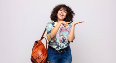 Neşeli bir şekilde gülümseyen ve yan taraftaki fotokopi alanını gösteren bir nesneyi gösteren veya reklamını yapan bir kadın.