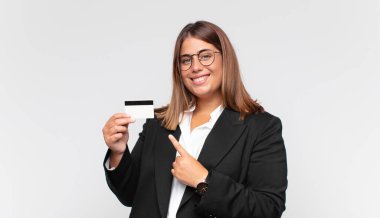 young woman with a credit card smiling cheerfully, feeling happy and pointing to the side and upwards, showing object in copy space
