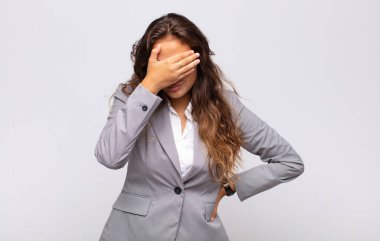 Stresli, utanmış ya da üzgün görünen bir kadın. Baş ağrısı var, yüzünü elleriyle kapatıyor.
