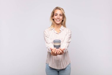 young woman with a coffee smiling happily with friendly, confident, positive look, offering and showing an object or concept
