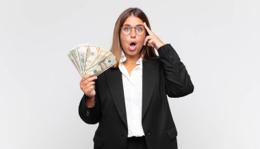 Banknotları olan genç bir kadın şaşırmış, ağzı açık, şok olmuş, yeni bir düşünce, fikir ya da konsept keşfediyor.