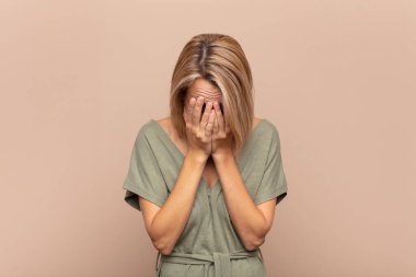 Üzgün, hayal kırıklığına uğramış, gergin ve depresif hisseden bir kadın. İki eliyle yüzünü kapatıyor, ağlıyor.