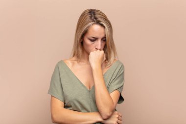 Kadın ciddi, düşünceli ve endişeli, elleri çenesine bastırılmış, yan bakıyor.