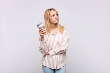 young woman with a coffee smiling happily and daydreaming or doubting, looking to the side