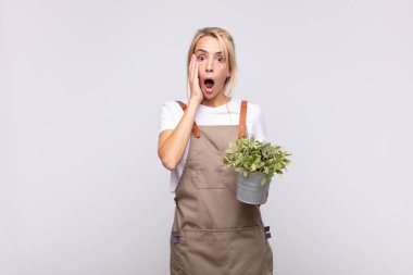 Genç kadın bahçıvan şok olmuş ve korkmuş hissediyor, ağzı açık ve elleri yanaklarında korkmuş görünüyor.