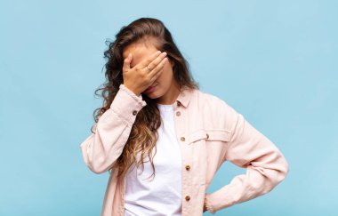 Stresli, utanmış ya da üzgün görünen bir kadın. Baş ağrısı var, yüzünü elleriyle kapatıyor.