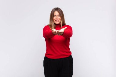 Genç sarışın kadın mutlu bir şekilde gülümsüyor arkadaş canlısı, kendinden emin, olumlu bakışlı, bir nesne ya da konsept sunuyor ve gösteriyor.