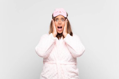 young woman wearing pajamas, feeling happy, excited and surprised, looking to the side with both hands on face