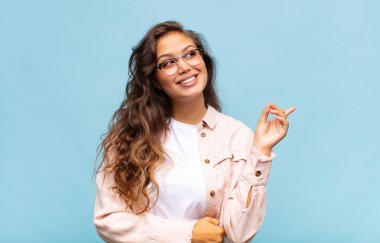 Kadın mutlu bir şekilde gülümsüyor ve yan bakıyor, merak ediyor, düşünüyor ya da bir fikri var.