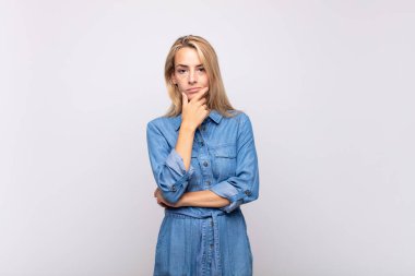 Ciddi, düşünceli ve güvensiz görünen bir kadın. Bir kolu çapraz ve eli çenesinde, seçenekleri değerlendiriyor.