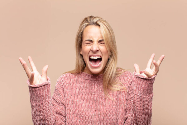 Женщина яростно кричит, чувствуя стресс и раздражение, подняв руки вверх и говоря, почему я