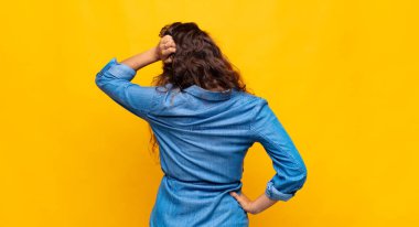 Kadın kendini cahil ve kafası karışık hissediyor, bir çözüm düşünüyor, eli kalçasında, diğeri kafasında, dikiz aynasından.