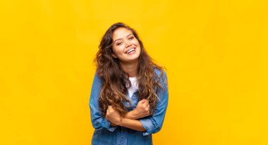 Neşeli bir şekilde gülümseyen ve yumruklarını sıkmış, kollarını kavuşturmuş, mutlu ve pozitif hisseden bir kadın.