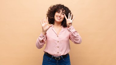 Gülümseyen ve arkadaş canlısı görünen bir kadın, 9 ya da 9 numarayı gösteriyor, eli önde, geri sayıyor.