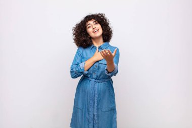 Bir kadın mutlu ve aşık, bir eli kalbinin yanında, diğer eli önde uzanmış gülümsüyor.