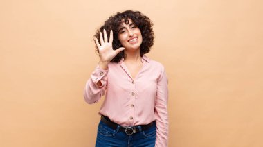 Gülümseyen ve arkadaş canlısı görünen bir kadın, 5 ya da 5 numarayı gösteriyor, eli önde, geri sayıyor.