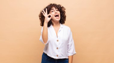 Kadın kendini başarılı ve tatmin olmuş hissediyor, ağzı açık gülümsüyor, elle işaret veriyor.