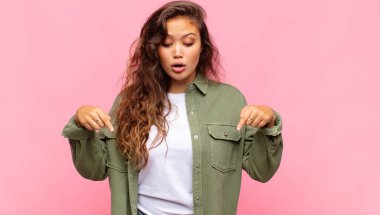 İki eliyle aşağıya doğru bakan ağzı açık bir kadın, şaşkın, şaşkın ve şaşırmış görünüyor.