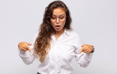 İki eliyle aşağıya doğru bakan ağzı açık bir kadın, şaşkın, şaşkın ve şaşırmış görünüyor.