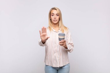 Elinde kahve olan genç bir kadın ciddi, sert, hoşnutsuz ve kızgın görünüyor.